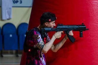 Боец LASERWAR в яркой футболке целится из оружия.
